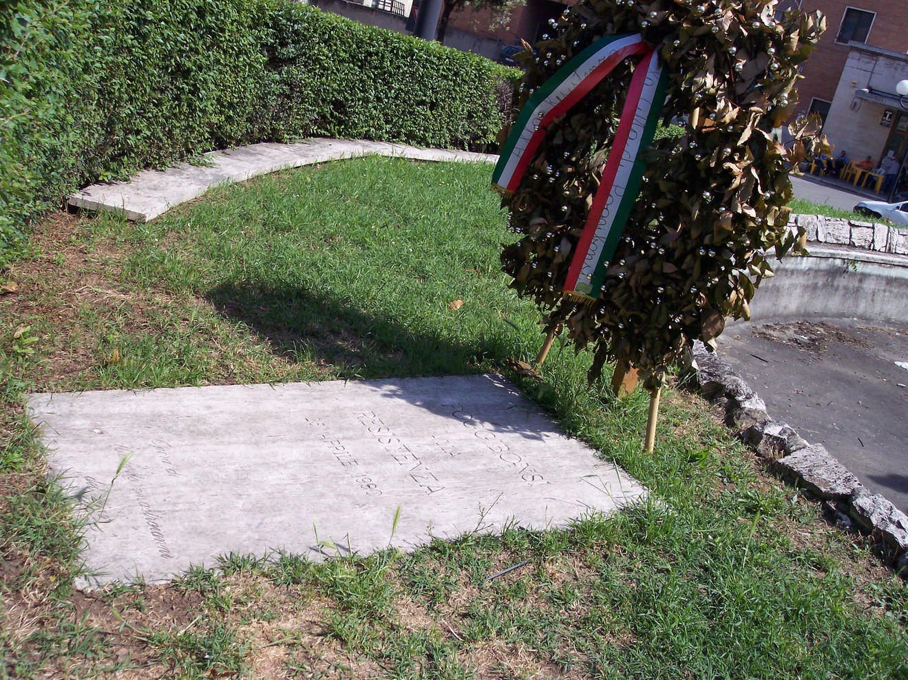 Monumento alla Resistenza, con corone di alloro e dettagli commemorativi immersi nel verde.