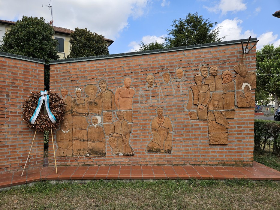 Monumento alla Resistenza con bassorilievi che raffigurano figure storiche e una corona d'alloro accanto.