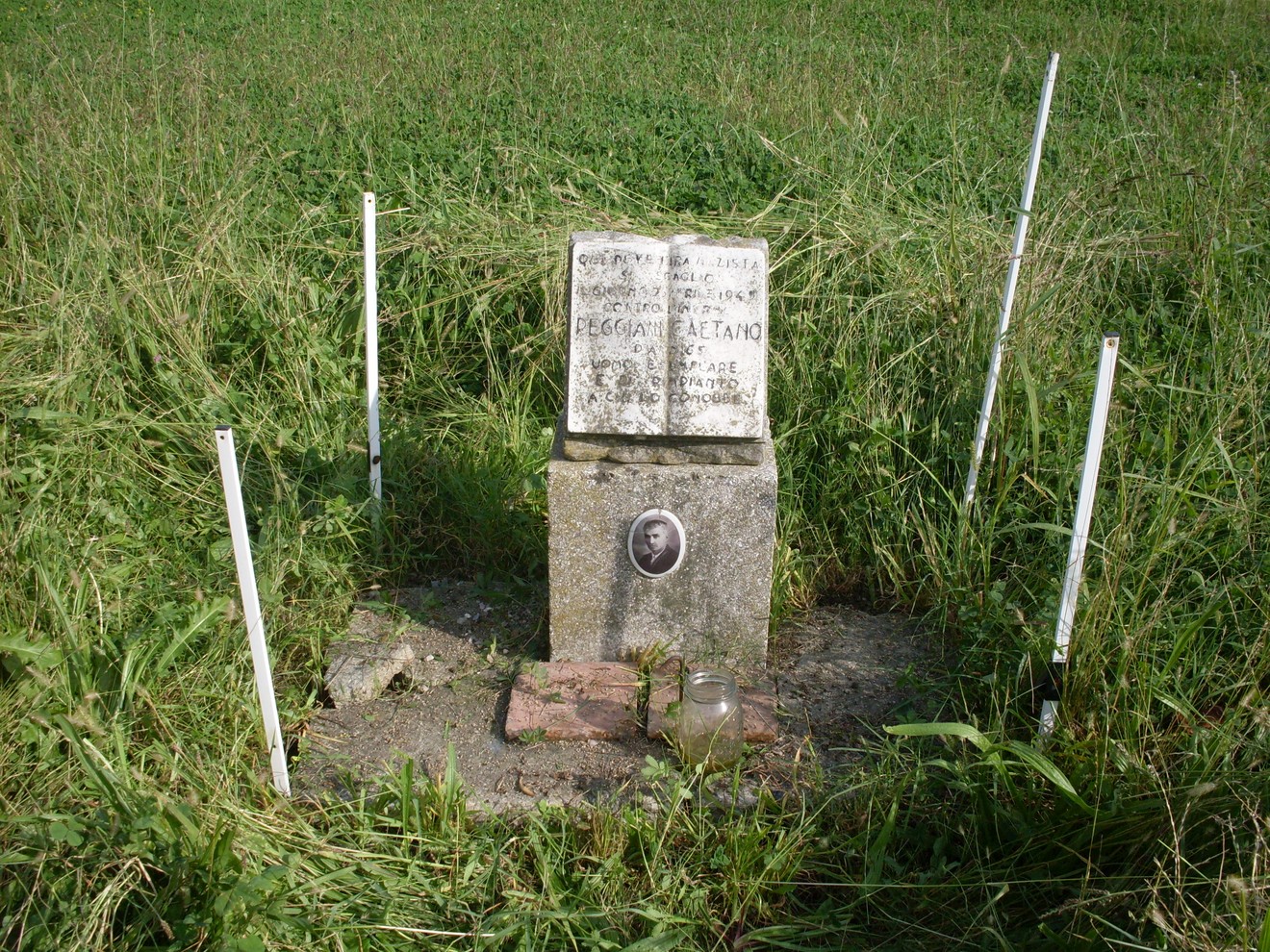Cippo commemorativo dedicato a Reggiani, immerse nel verde, con una fotografia e testo commemorativo.