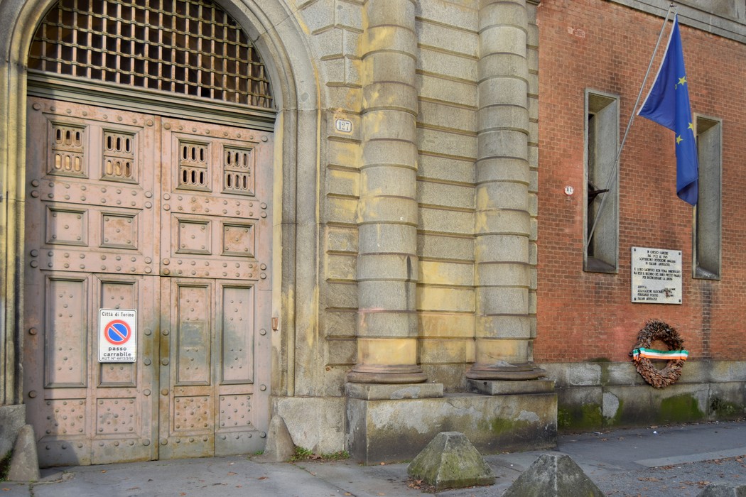 Lapide commemorativa ai detenuti antifascisti, con porta storica e decorazione floreale sul muro della prigione.