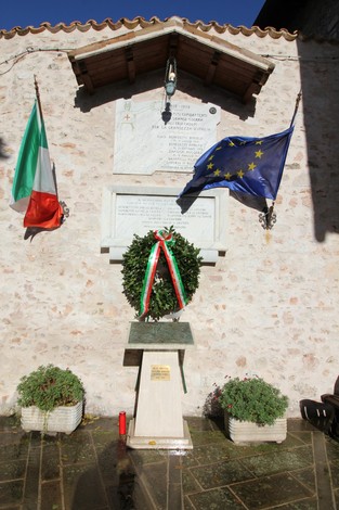 Lapidi commemorative per l'eccidio di Mucciafora, con bandiere italiana ed europea, in un contesto di rispetto e memoria.
