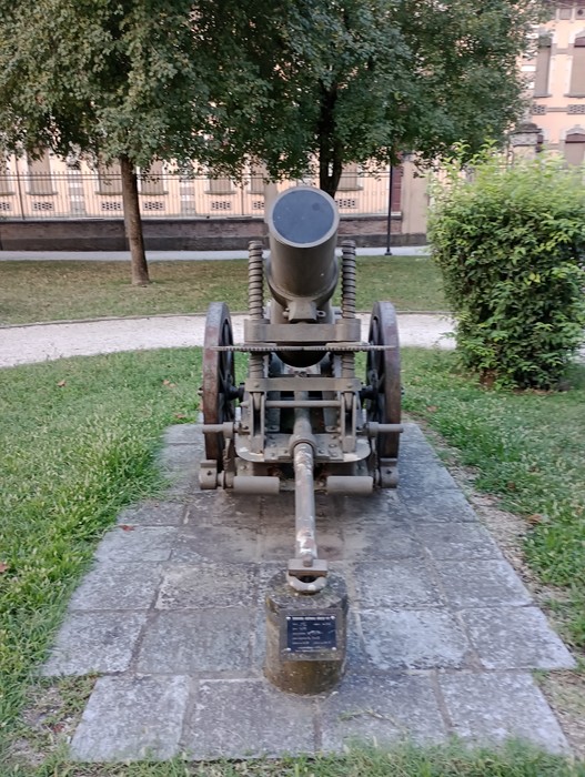 Monumento ai Caduti, cannone simbolico dedicato ai soldati delle guerre mondiali, immerso nel verde.