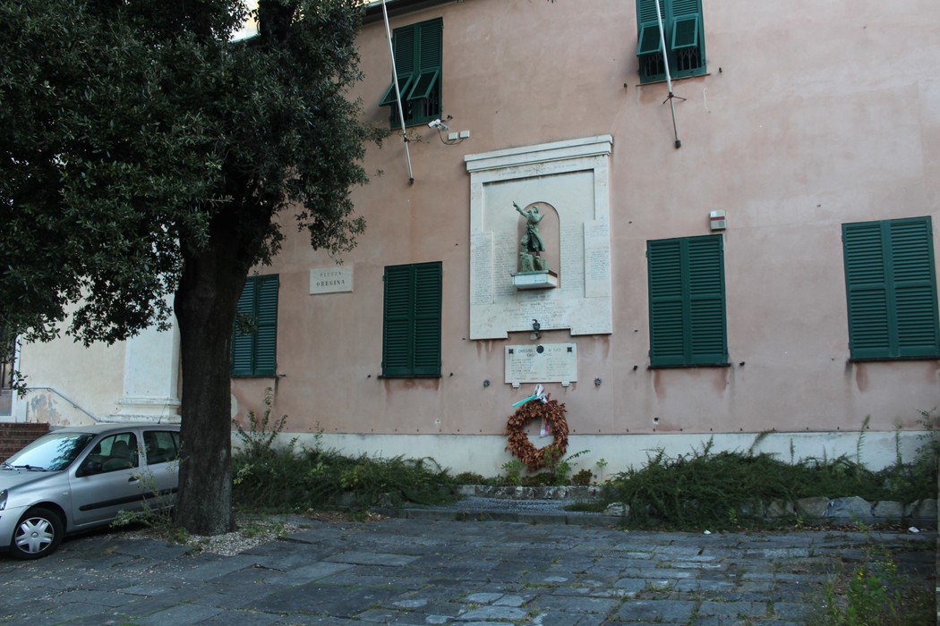 Lapidi commemorative ai caduti in un contesto urbano, con un monumento e un albero nelle vicinanze.