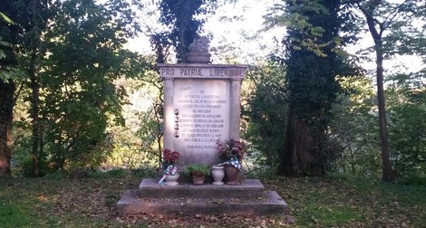 Cippo commemorativo dedicato ai martiri coneglianesi, immerso nel verde e circondato da piante.
