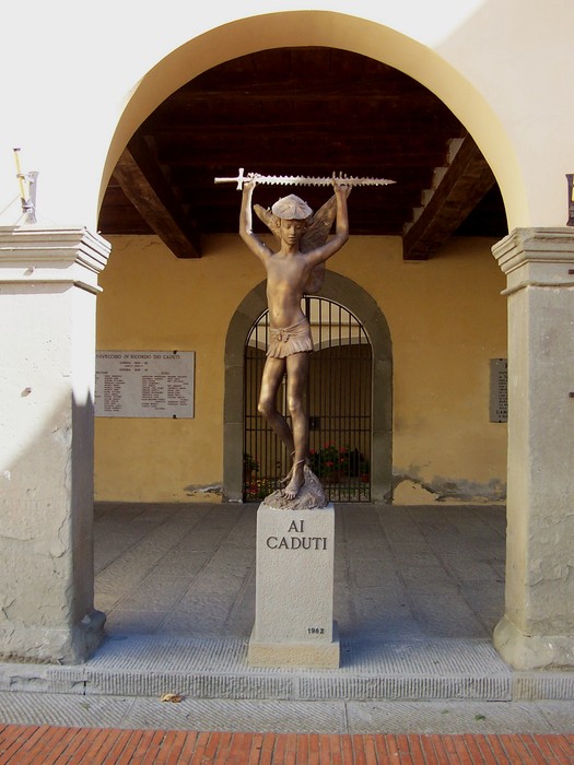 Statua commemorativa ai caduti di guerra, situata sotto un arco, con figura che regge una spada.