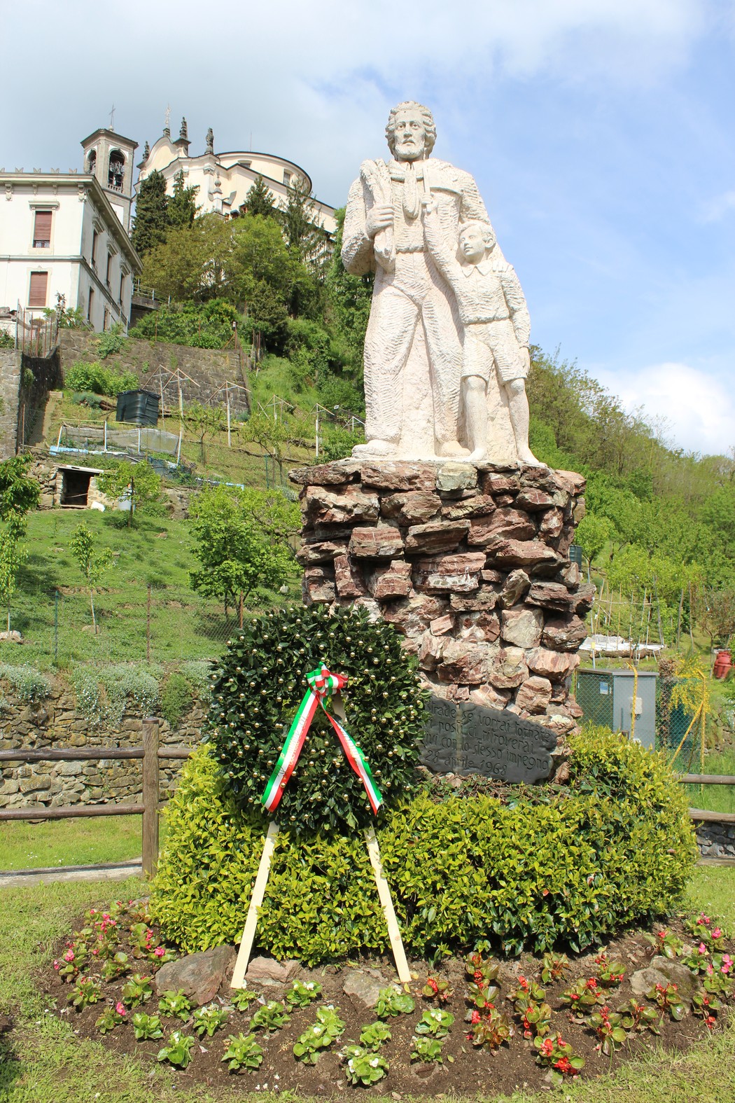 Monumento alla Resistenza con statue di figure storiche, circondato da fiori e vegetazione.