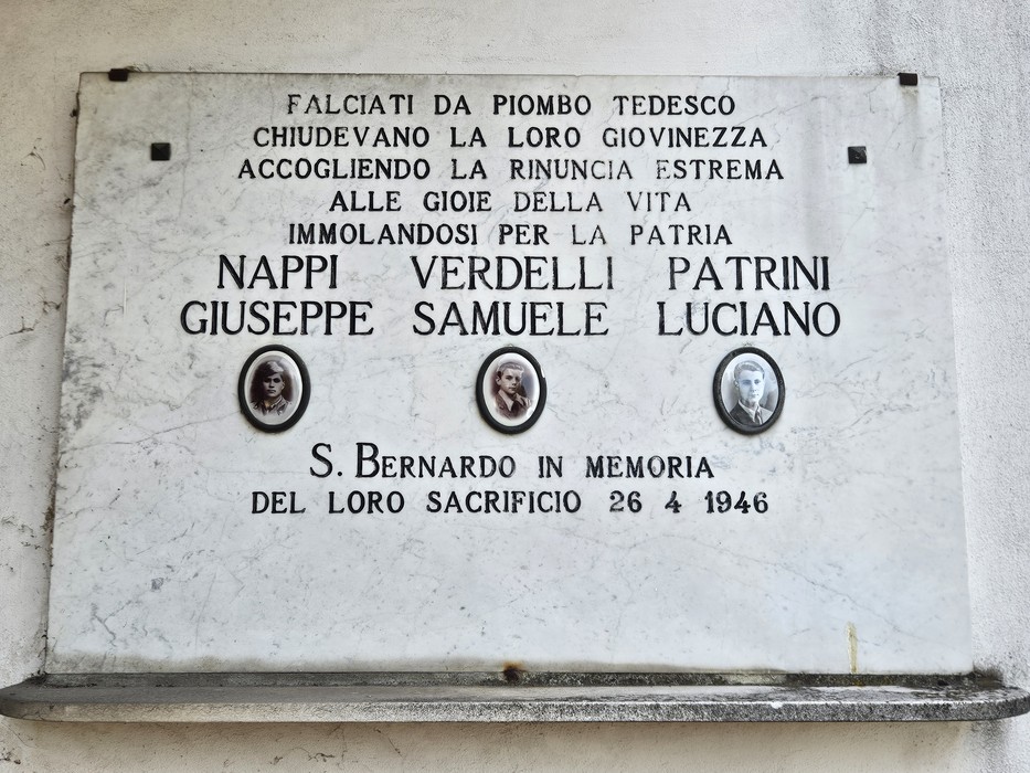 Lapide in marmo su parete, con iscrizione e tre ritratti ovali dei caduti ricordati.