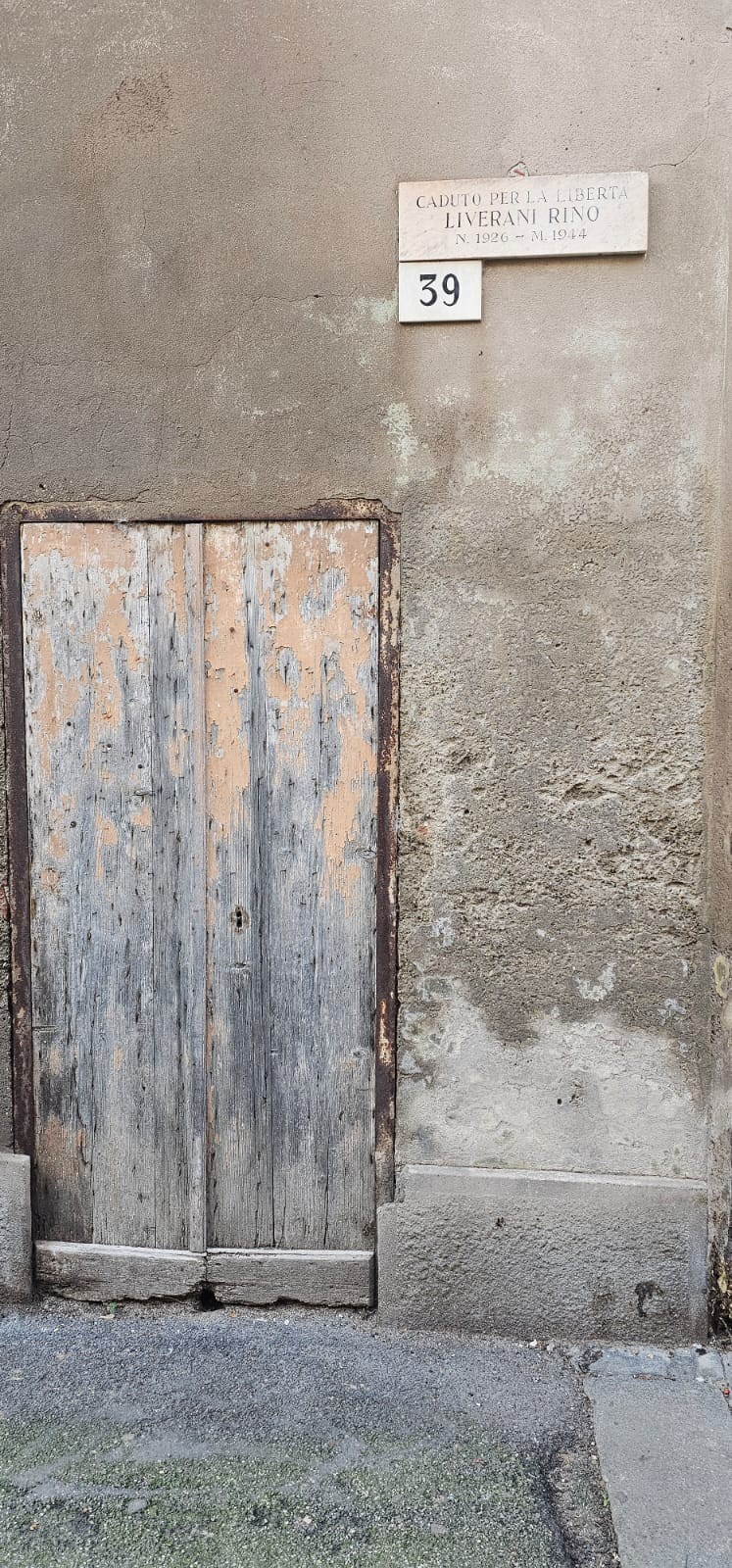 Lapide commemorativa in muratura con porta in legno usurata, situata su un muro di pietra.