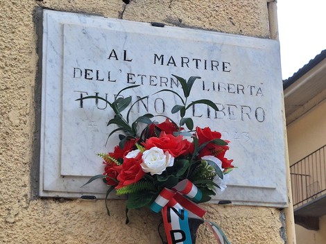Lapide commemorativa con fiori rossi e bianchi, dedicata a un martire della libertà.