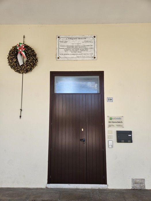 Lapide commemorativa a Fraccon affissa sopra una porta, con una ghirlanda decorativa accanto.