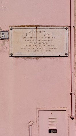 Lapide commemorativa dedicata a Lupi, affissa su una parete rosa.