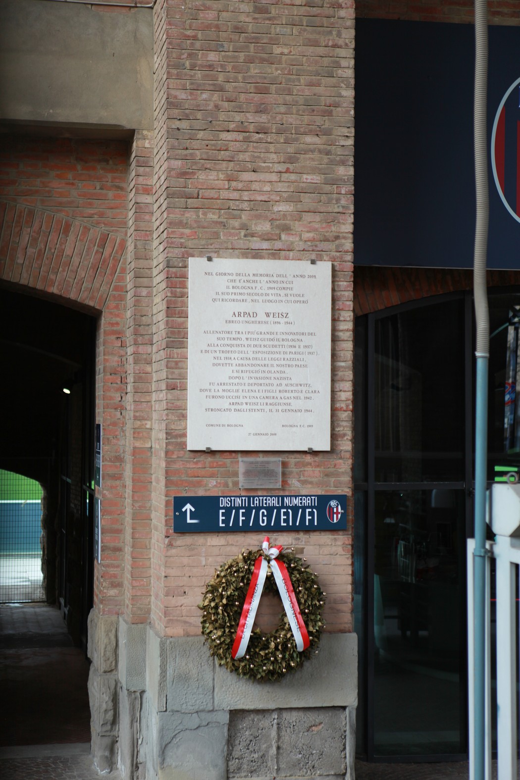 Lapide commemorativa a Weisz con corona di fiori, situata in un edificio caratteristico.