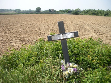 Croce commemorativa per i partigiani a Torretto, immersa in un campo, circondata da fiori.