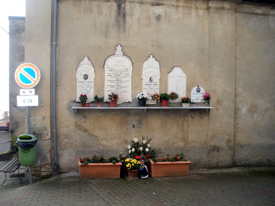 Lapide commemorativa con fiori e decorazioni, situata su un muro, in memoria di Molinari.