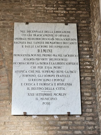 Lapide commemorativa in pietra, dedicata al decennale della Liberazione, con incisioni significative.