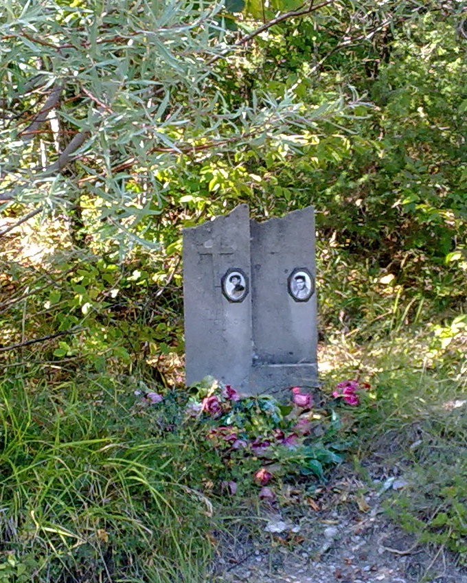 Cippo commemorativo dedicato a Zanni e Capitani, circondato da vegetazione e fiori.