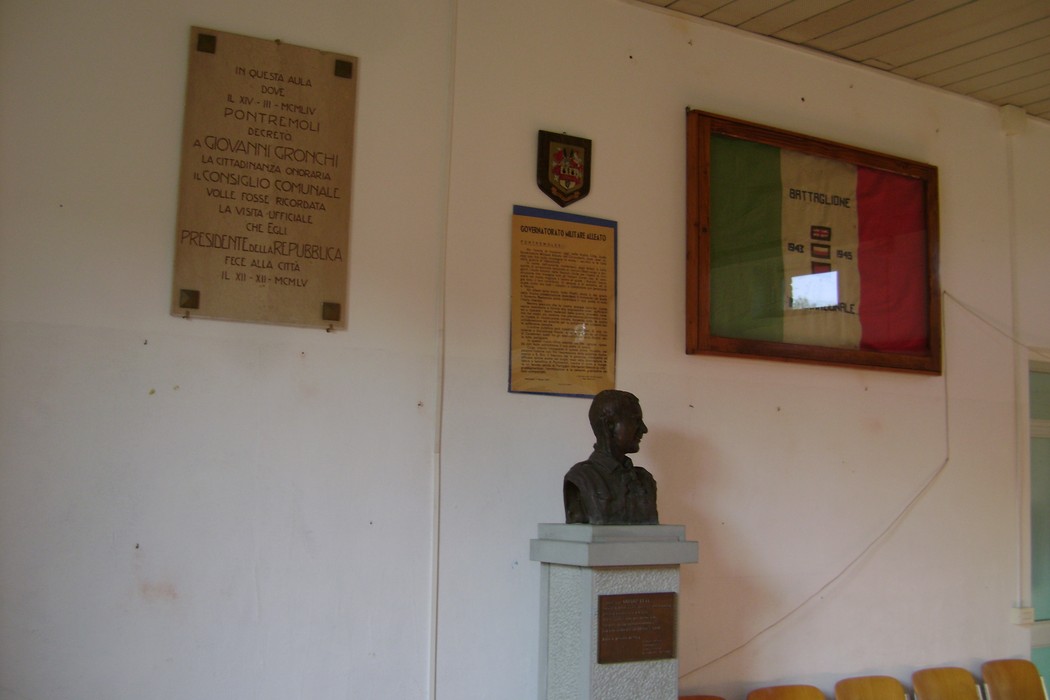 Busto di un personaggio storico, collocato in un ambiente con alcune targhe commemorative e insigni nazionali.