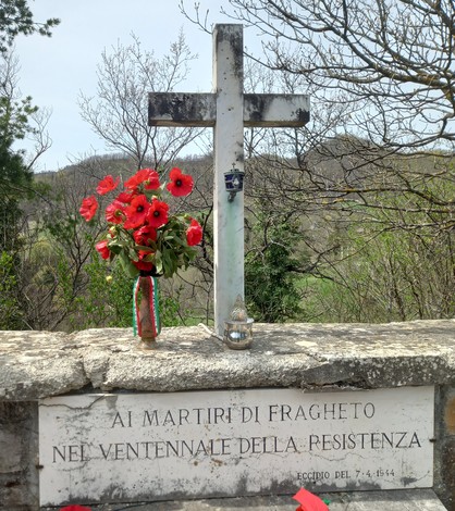 Cenotafio dedicato ai martiri di Fragheto, con fiori rossi e una croce, situato in un contesto naturale.