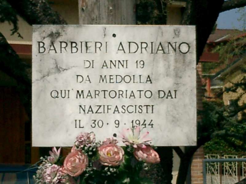 Targa commemorativa in memoria di Barbieri Adriano, martire antifascista del 30 settembre 1944, adornata con fiori.