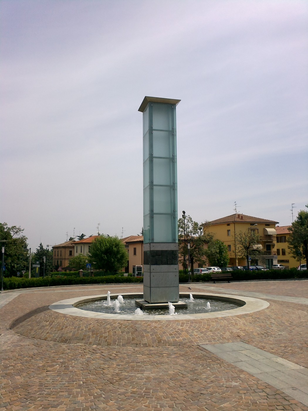 Monumento alla pace con obelisco trasparente e fontane, situato in un'area urbana tranquilla.
