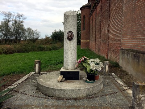 Cippo commemorativo a Genestrone, decorato con fiori e situato in un'area tranquilla.