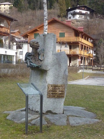 Monumento a Collini: scultura commemorativa in pietra, situata in un contesto naturale, tra edifici storici.