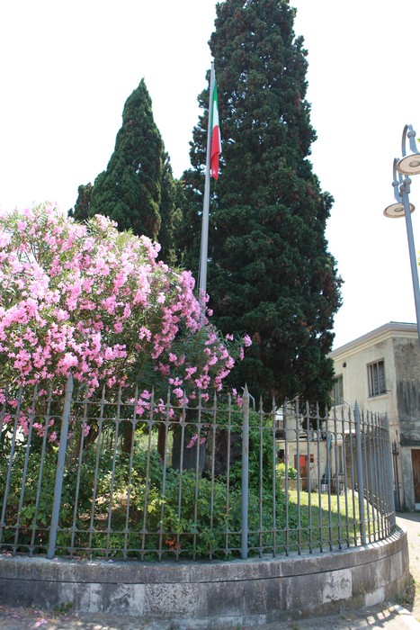 Il Monumento ai caduti del Lido circondato da fiori e alberi, con una bandiera italiana ben visibile.