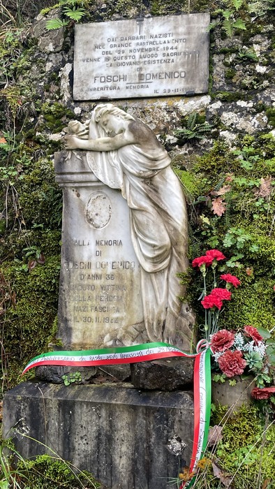 Monumento a Foschi con statua e lapide commemorativa, arricchito da fiori e nastri tricolori.