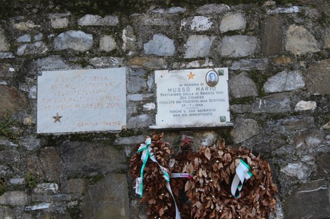 Lapide commemorativa a Severino, con dedica e omaggio floreale, in un contesto di pietra e natura.