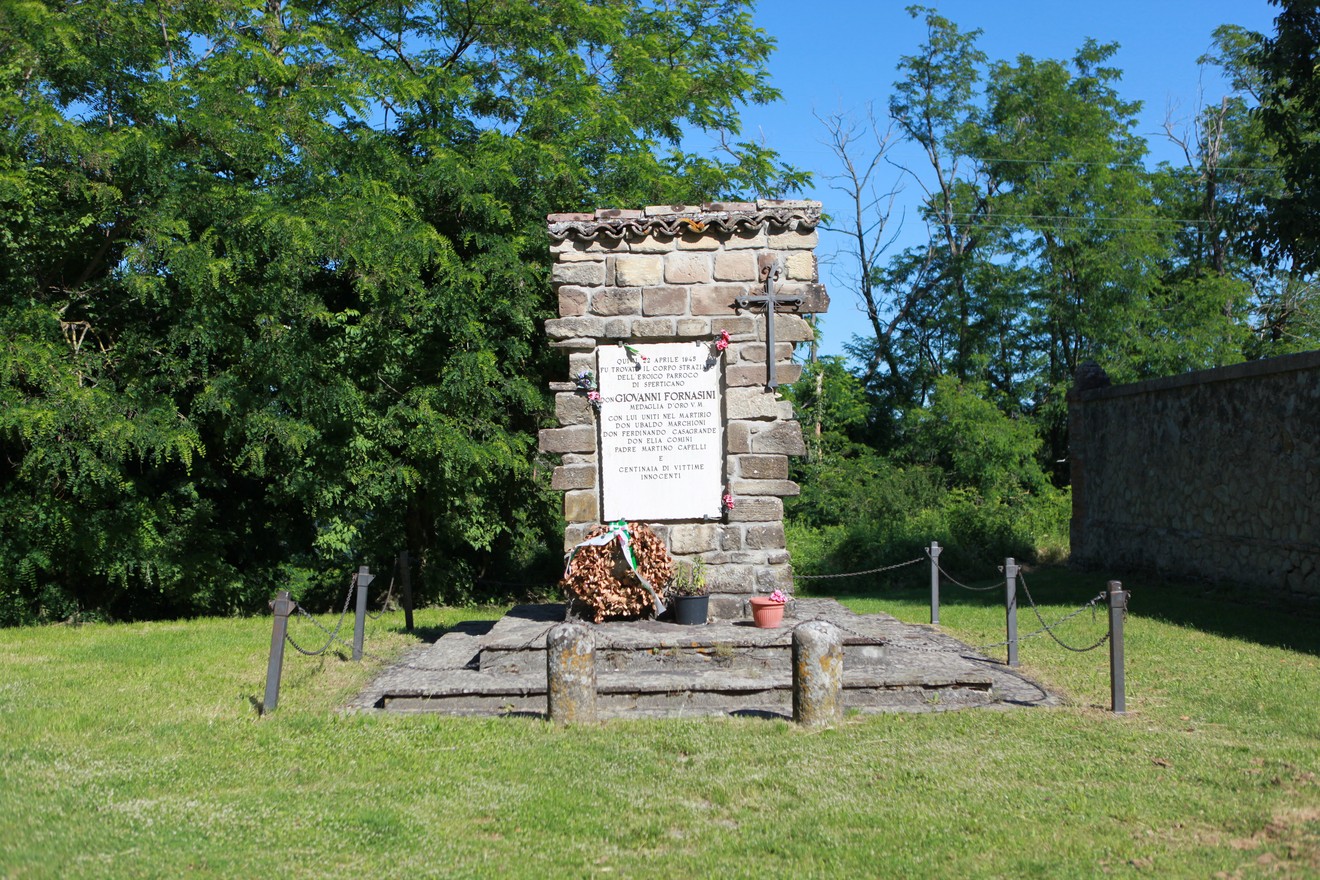 Monumento commemorativo dedicato a Fornasini e altri, immerso nel verde, con decorazioni floreali.