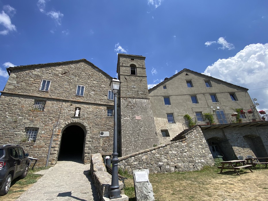 Targa ai Rossi, vista di edifici in pietra con campanile, immersi nel verde sotto un cielo azzurro.