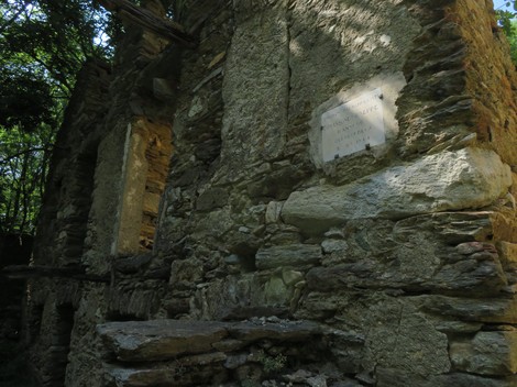 Lapide in pietra su una parete di una rovina, circondata da vegetazione lussureggiante.