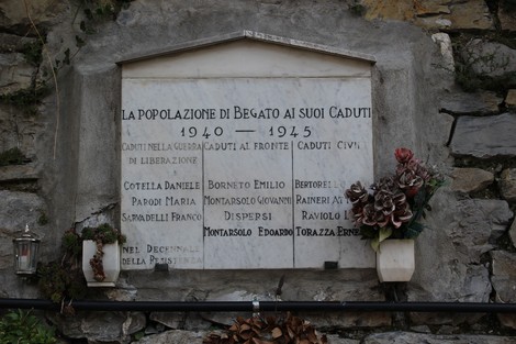 Lapide commemorativa dedicata ai caduti di Begato durante la Seconda Guerra Mondiale, con fiori e decorazioni.