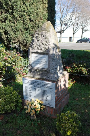 Monumento commemorativo alla Brigata Bolero, con una pietra e fiori in un'area verde.