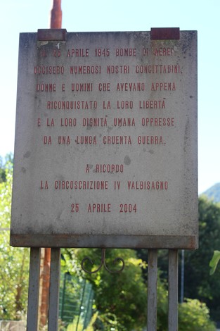 Lapide commemorativa dedicata alle vittime del bombardamento del 1945, situata in un contesto naturale.