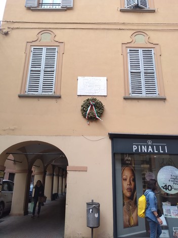 Lapide commemorativa ad Allegretti collocata su una facciata con decorazioni e corona di alloro.
