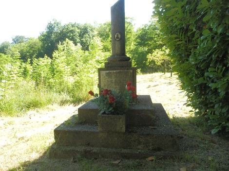 Cippo commemorativo circondato da vegetazione e fiori rossi in un ambiente naturale.