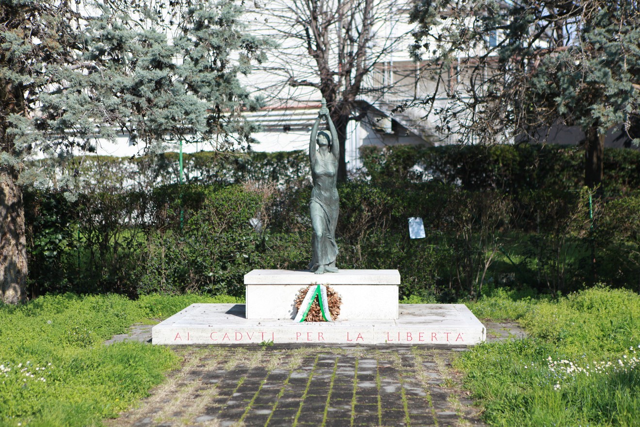 Monumento alla 63° Brigata Garibaldi, con statua e composizione floreale su base marmorea, immerso nel verde.