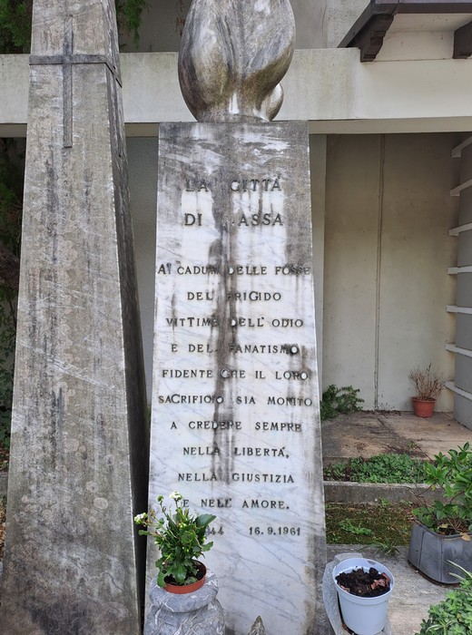 Stele in marmo con iscrizione, sormontata da una scultura, all'aperto vicino a una croce in pietra.