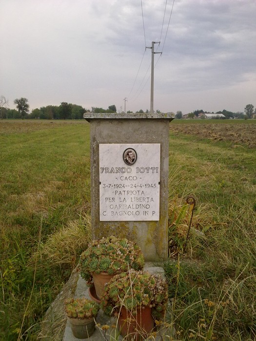 Cippo commemorativo dedicato a Franco Lotti, patriota per la libertà, con piante ornamentali circostanti.