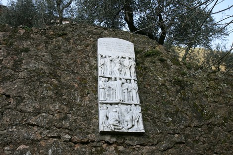 Lapide in memoria dei caduti di Valdicastello, incastonata in una roccia circondata da olivi.