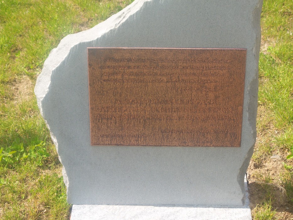 Cippo commemorativo in pietra, dedicato a Kayser, immerso in un prato verde.