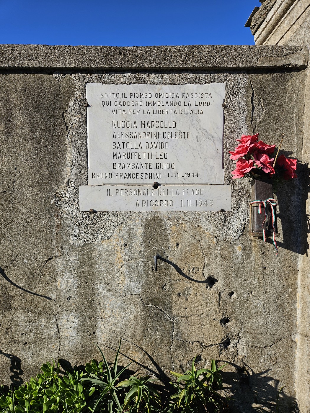 Lapide commemorativa ai Martiri della FLAGE, con testo inciso e fiori in omaggio.