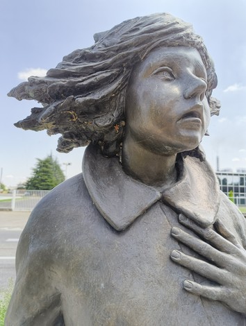Scultura di bronzo che ritrae una giovane ragazza con i capelli al vento, esprimendo emozione e dignità.