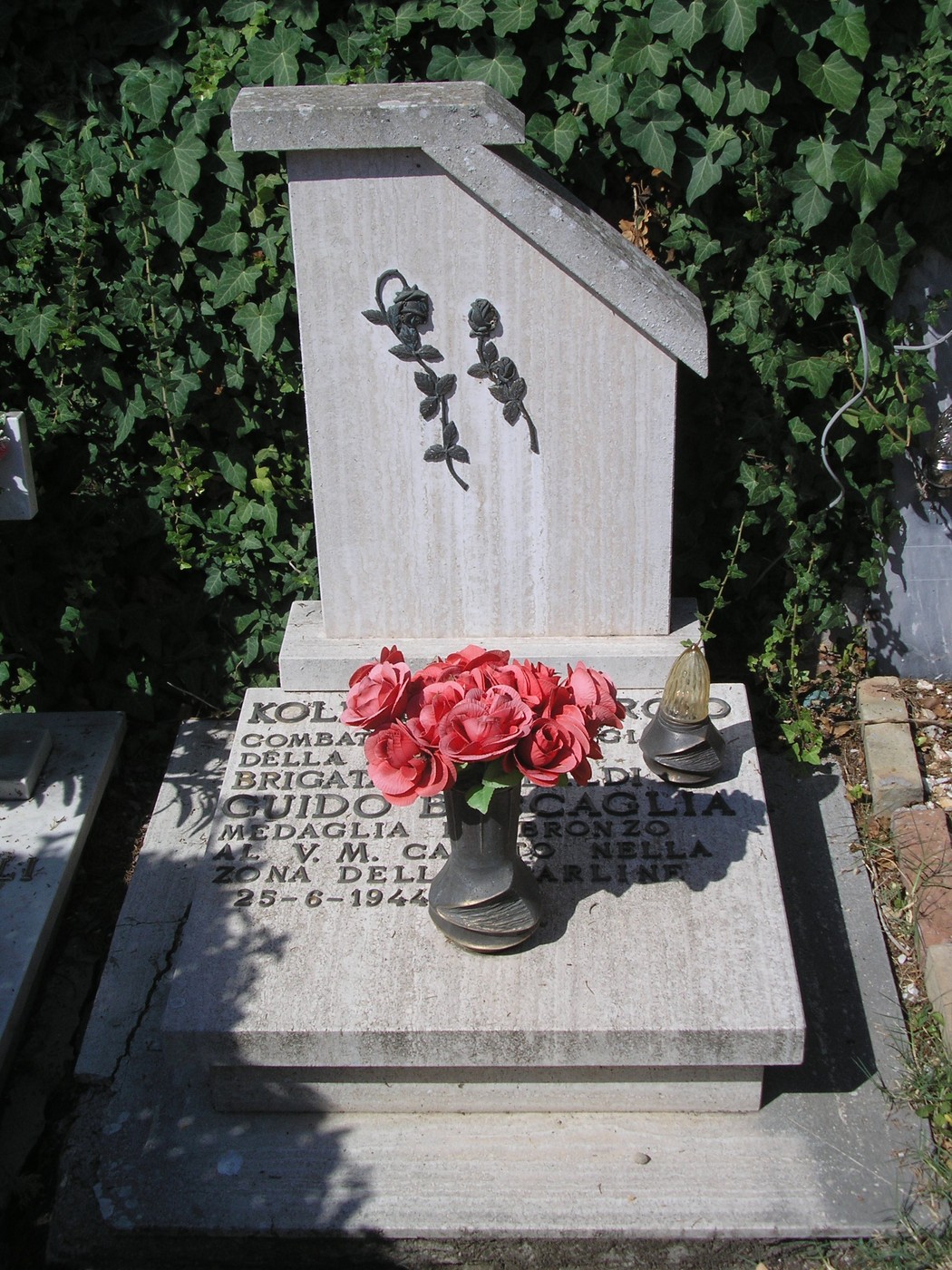 Tomba di Kolesian con decorazioni floreali e monumento commemorativo in un contesto di giardino.