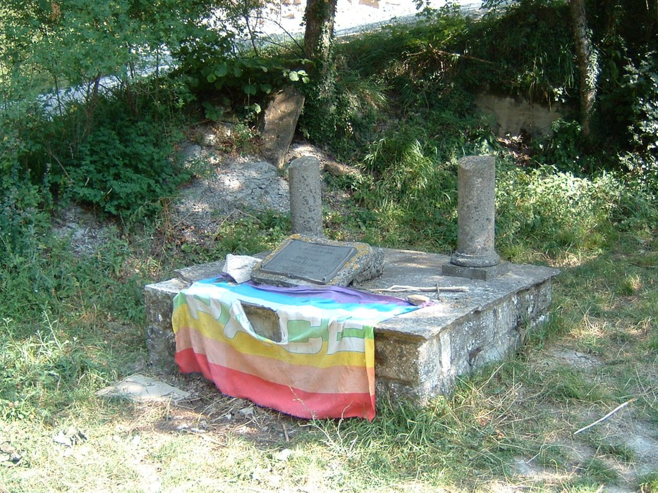 Monumento a Neri e Bellenghi, con una base in pietra e una bandiera colorata. Natura circostante.