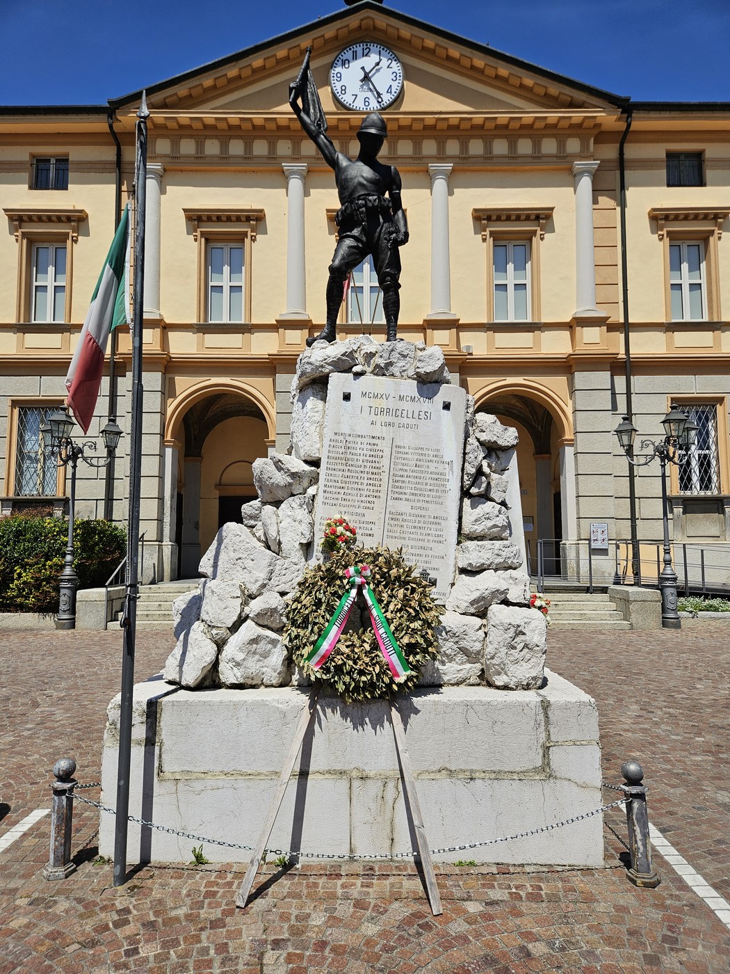 Monumento ai Caduti con statua di soldato, candelabri e decorazioni floreali in una piazza storica.