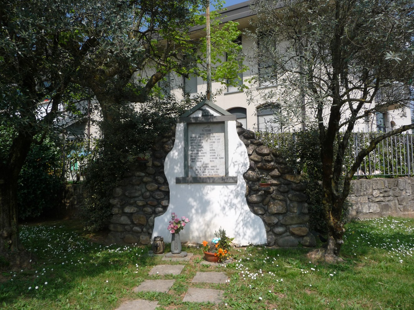 Lapide commemorativa ai caduti partigiani, con decorazioni floreali e un contesto naturale di alberi e prato.