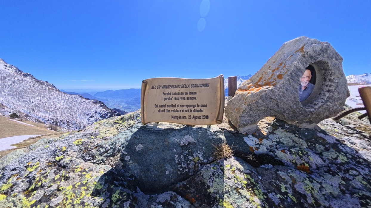 Targa in pietra con iscrizione su un masso in alta quota, accanto a una roccia forata con una foto all'interno.