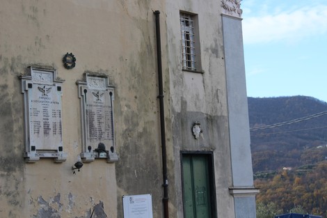 Lapide commemorativa ai caduti, con due tabelle incastonate su un muro, contesto montano e vegetazione autunnale.